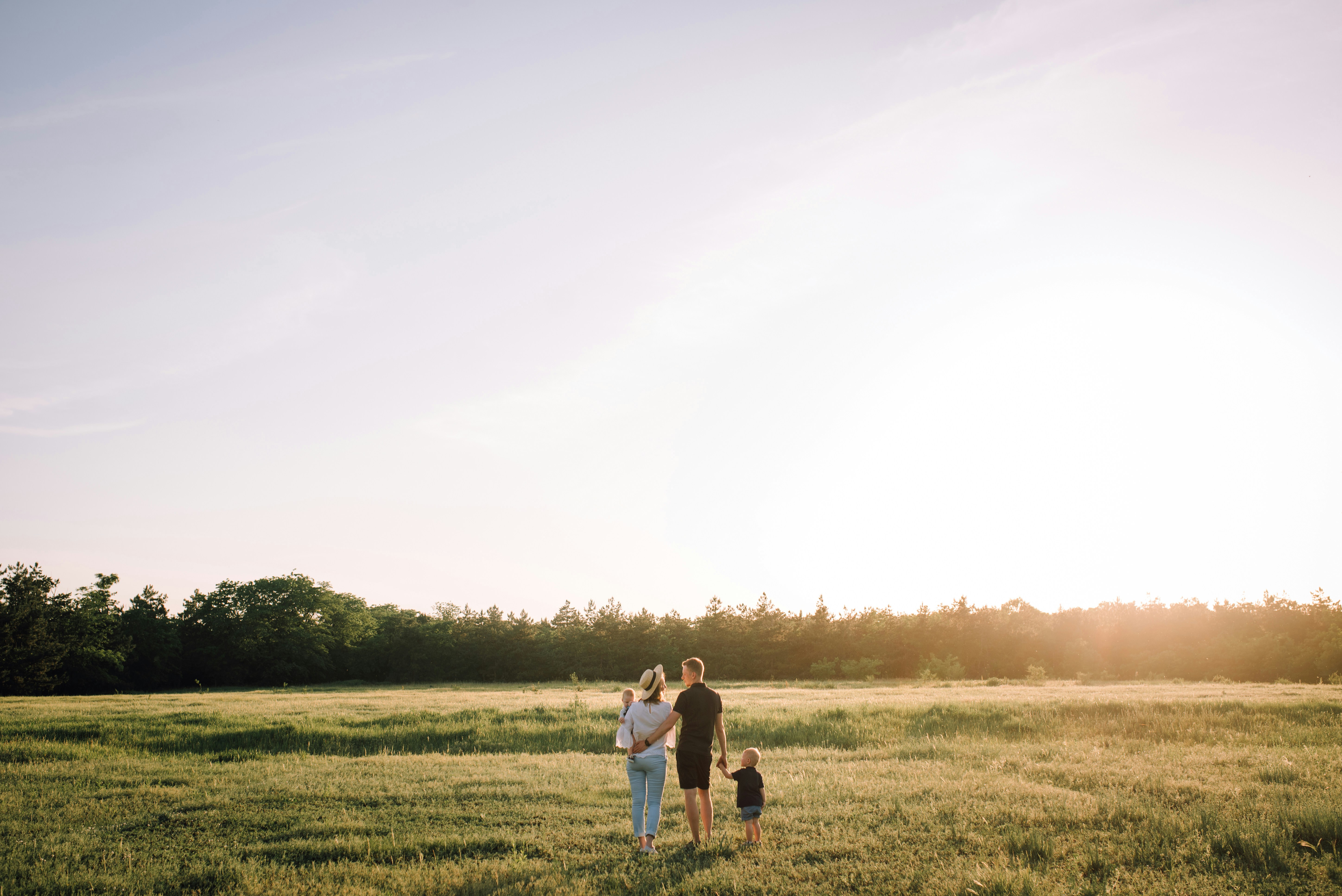 Family of three walking together across an open field at golden hour